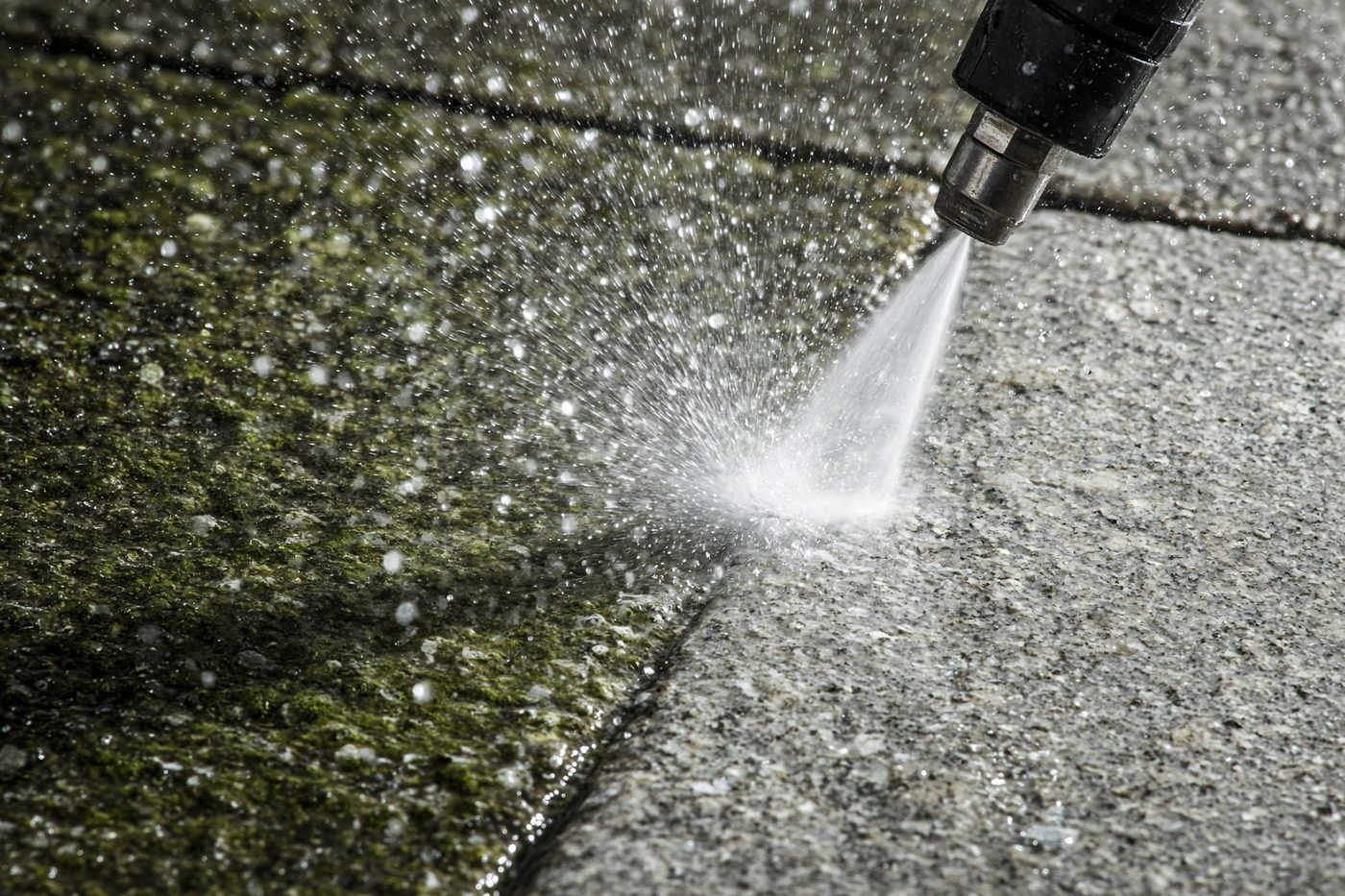 Close-up of a pressure washer nozzle blasting algae off paving